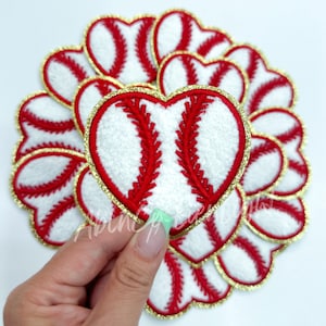 May include: A group of 10 red and white baseball-themed heart-shaped patches with gold glitter trim. The patches are made of a soft, fuzzy material.