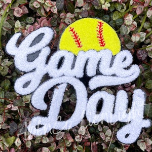May include: White and black felt letters spelling "Game Day" with a yellow softball with red stitching on top.