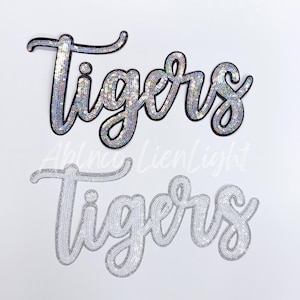 May include: Two silver sequined iron-on patches that spell out the word "Tigers".