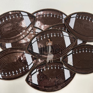 May include: A group of seven brown and white football-shaped patches with sequins. The patches are made of brown sequins with white stitching and white accents.