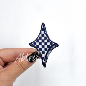 May include: A blue and white checkered star-shaped iron-on patch. The patch is made of fabric and has a shiny finish.