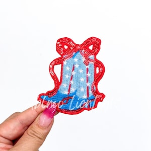 May include: A red, white, and blue sequined bell with a red bow. The bell is decorated with white stars on a blue background.