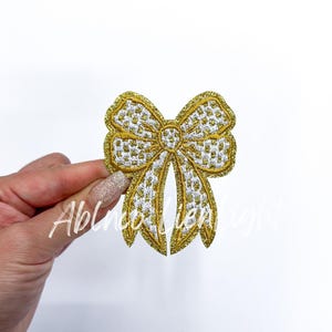 May include: A gold glitter bow with a white checkered pattern. The bow is a decorative embellishment for crafts and clothing.