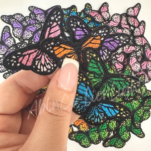 May include: A collection of colorful embroidered butterfly patches. The patches are in various colors, including pink, orange, green, blue, and purple. The patches are all different sizes and shapes, and they are arranged in a random pattern.