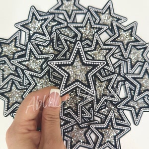 May include: A pile of silver and black star-shaped patches with rhinestones. The patches have a white outline and are sewn with small white beads.