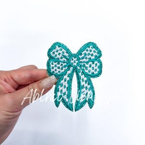 May include: A teal blue bow with a white checkered pattern. The bow is made of fabric and has a glittery finish.