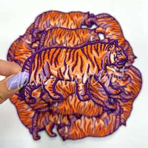 May include: A stack of orange and purple embroidered iron-on patches featuring a tiger design.