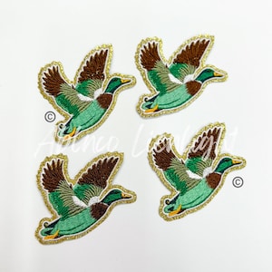 May include: Four green and brown embroidered iron-on patches of flying ducks with gold glitter trim.