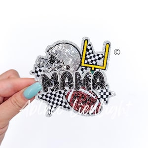 May include: A black and white checkered fabric patch with the word "MAMA" in black beads. The patch also features a silver sequin football helmet, a red and white football, and a yellow goal post.