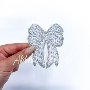 May include: A silver glitter bow with a checkered pattern. The bow is a decorative embellishment for crafts and clothing.