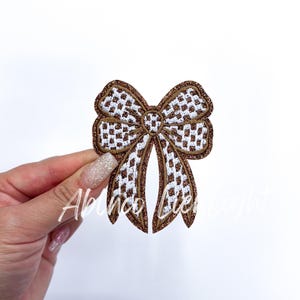 May include: A brown and white checkered bow with a glittery finish. The bow is made of fabric and has a slightly raised texture.