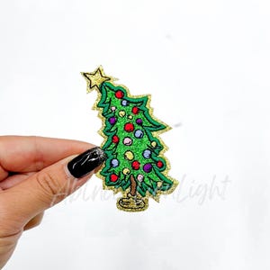 May include: A green glitter Christmas tree with a gold star on top and colorful ornaments. The tree is on a gold glitter base.