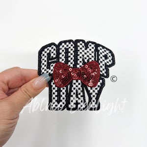 May include: Black and white checkered iron-on patch with the text "COMP DAY" and a red sequined bow.