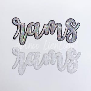 May include: Two iron-on patches with the word "rams" in a cursive font. The top patch is silver with iridescent sequins and a black outline. The bottom patch is white with silver sequins.