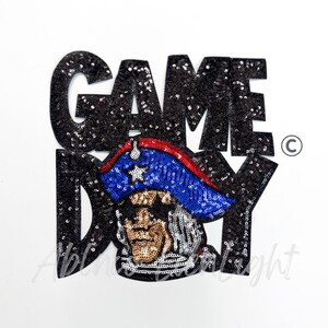 May include: A sequined patch with the words "GAME DAY" in black sequins. The patch features an image of a man in a tricorn hat with a blue and red brim. The man's face is detailed with sequins.