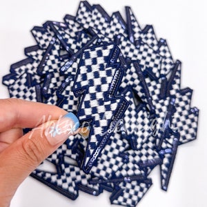 May include: A stack of blue and white checkered lightning bolt patches. The patches are made of fabric and have a shiny finish.