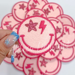 May include: A pile of pink felt iron-on patches with a smiley face, a lightning bolt, and a glitter star.