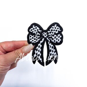 May include: Black and white checkered bow applique. The bow is made of fabric and has a shiny finish.