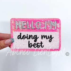 May include: Pink and white name tag with silver glitter lettering that says "Hello I'm doing my best".