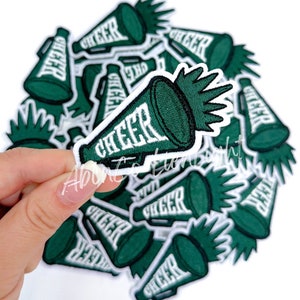 May include: A pile of green and white iron-on patches shaped like megaphones with the word "CHEER" written on them.