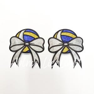 May include: Two white glitter bows with a blue and gold volleyball design in the center.