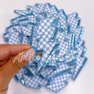 May include: A stack of blue and white checkered lightning bolt iron-on patches with a blue sequin border.