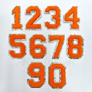 May include: Set of ten orange felt iron-on numbers with a silver outline. The numbers are 1, 2, 3, 4, 5, 6, 7, 8, 9, and 0.