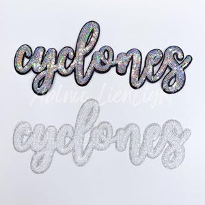 May include: Two versions of the word "cyclones" in silver sequins. The top version is black with iridescent sequins. The bottom version is white with silver sequins.