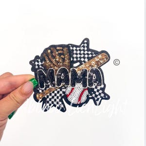 May include: A black and white checkered fabric patch with the word "MAMA" in black sequins. The patch also features a baseball, a baseball bat, and a baseball glove, all made of sequins.