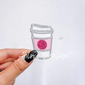 May include: White and silver embroidered coffee cup patch with a pink glitter circle in the center.