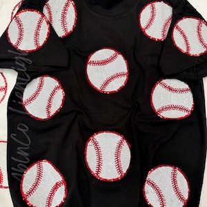 May include: Black t-shirt with red and white baseballs made of sequins. The baseballs are scattered across the shirt.