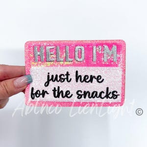 May include: Pink and white iron-on patch with the text "Hello I'm just here for the snacks".