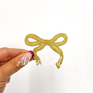 May include: A gold glitter bow applique. The bow is a simple design with two loops and a center knot.