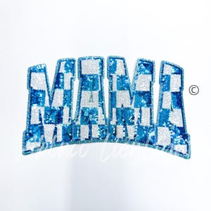 May include: A blue and white sequined patch in the shape of the word "MAMA". The letters are in a checkerboard pattern, with a curved bottom edge. The patch is on a white background.