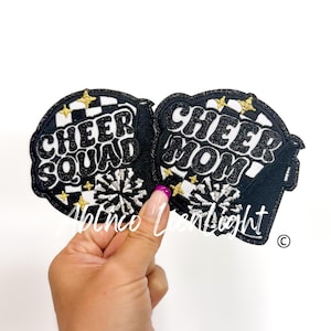 May include: Two black and white iron-on patches with gold glitter accents. One patch says "Cheer Squad" and the other says "Cheer Mom".