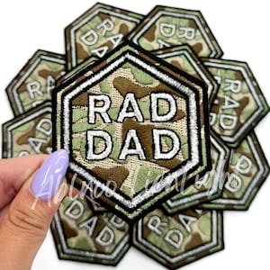 May include: A stack of ten iron-on patches in a camouflage pattern with the text "RAD DAD" in white. The patches are shaped like hexagons with a white border.