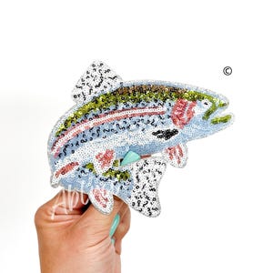 May include: A sequined trout fish patch in shades of blue, green, pink, and white. The fish is in a jumping position with its tail raised.
