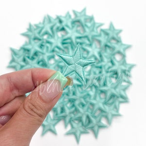 May include: A pile of light blue felt star-shaped patches. The stars are about 1 inch in diameter.