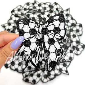May include: Black and white soccer ball patterned fabric bow. The bow is made of a glittery fabric and is perfect for adding a touch of sportiness to any project.