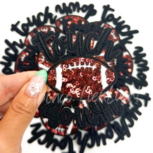 May include: A close-up of a red and white sequined football with the words "touch down" in black embroidery. The football is surrounded by several other patches with the words "touch down" in black embroidery.