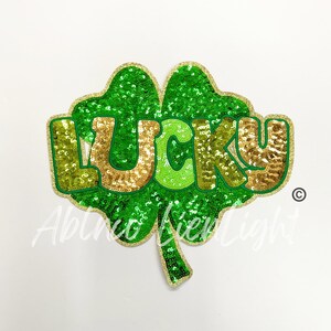 May include: A green and gold sequined iron-on patch shaped like a four-leaf clover with the word "LUCKY" in gold sequins.