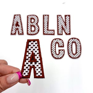 May include: A set of brown and white checkered fabric letters that spell out "ABLNA CO". The letters are individually cut out and have a white background with brown checkered squares.