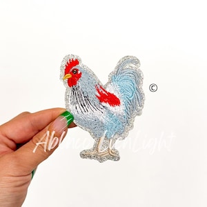 May include: A silver glitter iron-on patch featuring a blue and white rooster with a red comb and wattle.