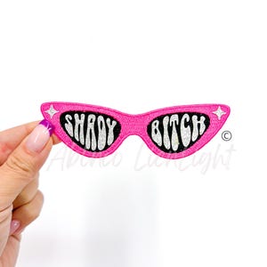 May include: Pink fabric patch with a pair of sunglasses that say "Shady Bitch" in white glitter letters.