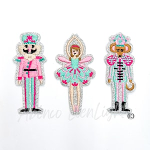 May include: Three embroidered iron-on patches featuring characters from the Nutcracker: a pink and green Nutcracker soldier, a green and pink ballerina, and a pink and green mouse king.