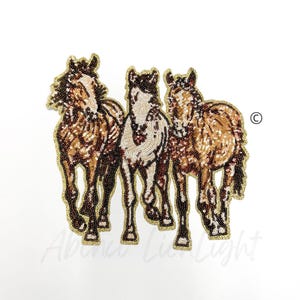 May include: Three brown and white horses with gold sequin details. The horses are standing side by side and are facing forward. The horses are on a white background.