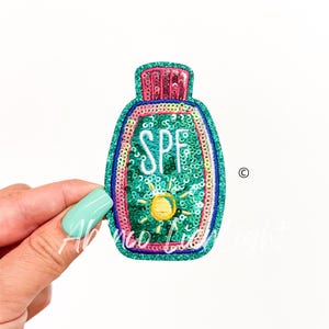 May include: A green, pink, and blue sequin patch shaped like a bottle of sunscreen with the word "SPF" and a yellow sun embroidered on it.