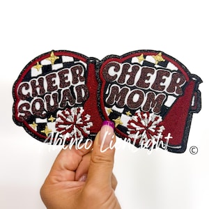 May include: Two iron-on patches with black and white checkered backgrounds and red and white pom-poms. One patch says "Cheer Squad" and the other says "Cheer Mom".