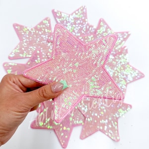 May include: A set of pink star-shaped patches covered in iridescent sequins. The patches are approximately 3 inches in diameter.