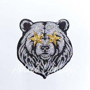May include: A black and silver sequined bear face with gold star-shaped sequins over the eyes.